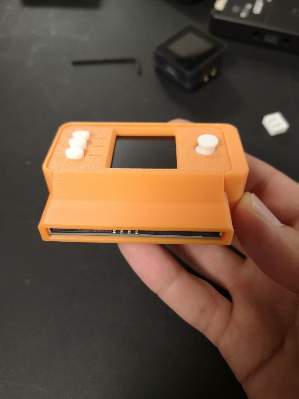 The assembled orange 3D-printed SeedSigner enclosure held in one hand, with the smartcard slot visible along the bottom edge.